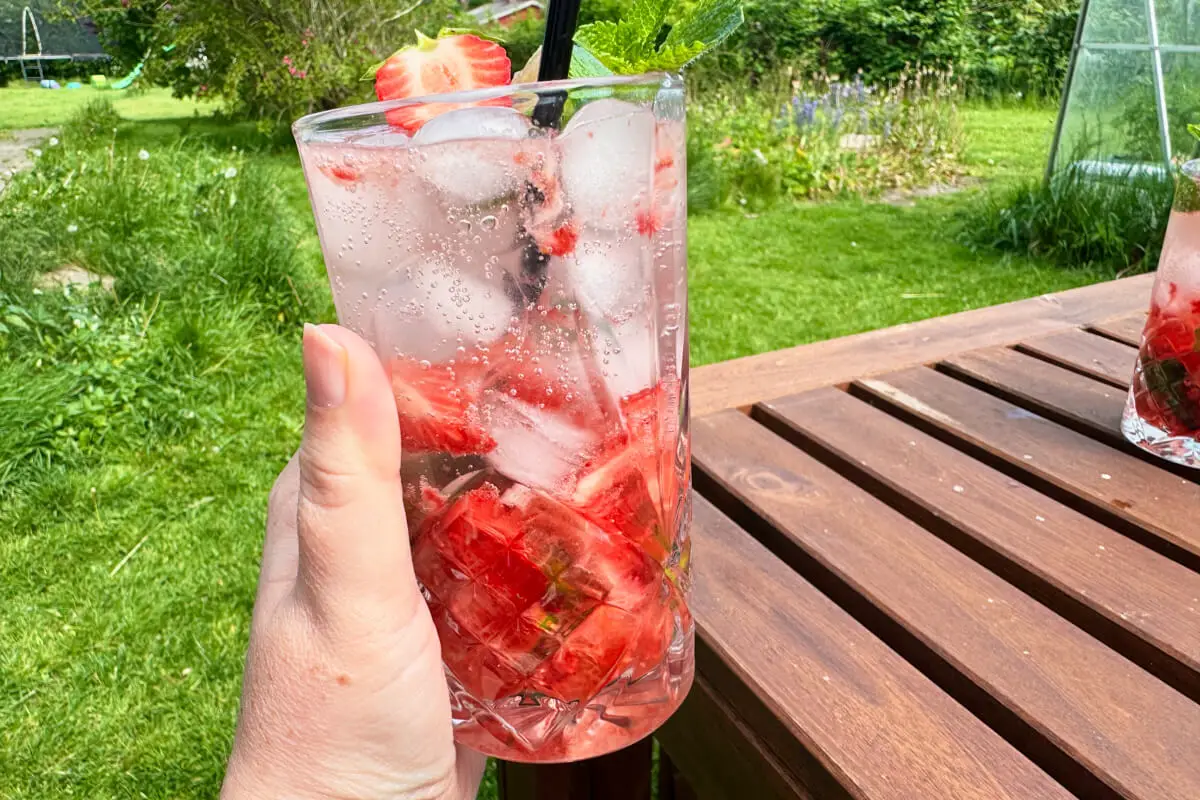 hånd med glas med jordbær mojito i en have.