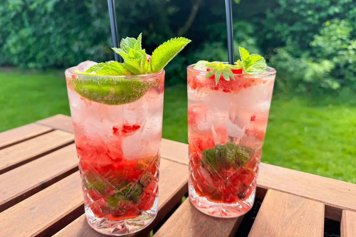 jordbær mojito i høje glas  pyntet med lime, mynte og jordbær på et havebord i sommervejret.